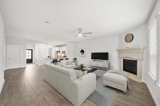 living area with visible vents, light wood-style flooring, a ceiling fan, and a glass covered fireplace