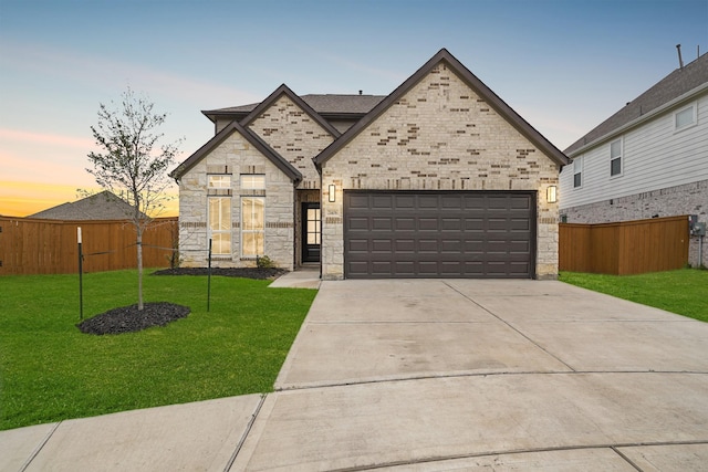 french provincial home with stone siding, fence, concrete driveway, an attached garage, and a front yard