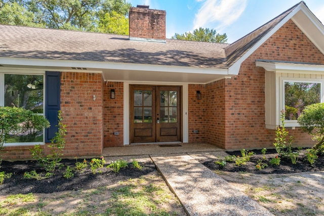 doorway to property featuring french doors, brick siding, roof with shingles, and a chimney