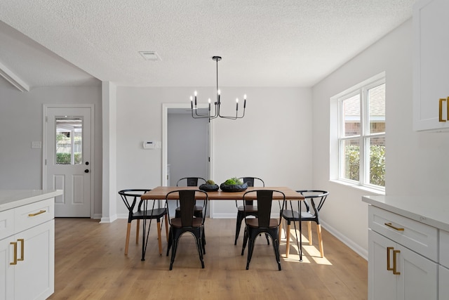 dining space featuring baseboards, a notable chandelier, a textured ceiling, and light wood-style floors