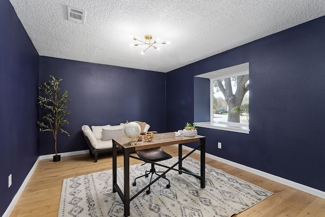 office area with baseboards, wood finished floors, visible vents, and a textured ceiling