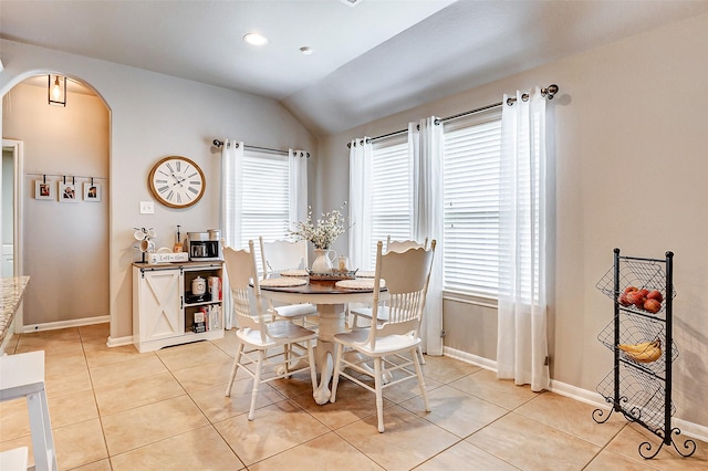 dining space featuring baseboards, arched walkways, light tile patterned flooring, and vaulted ceiling