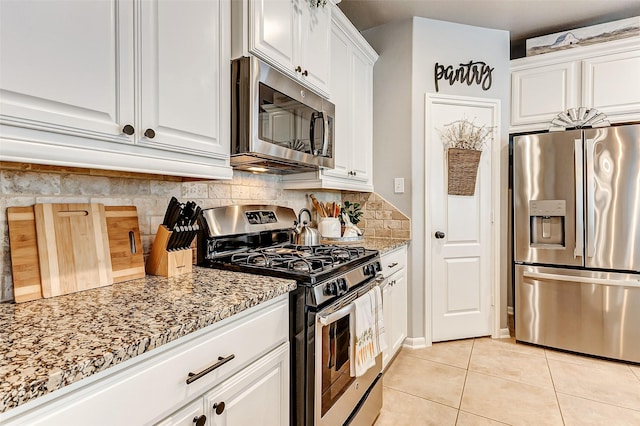 kitchen with light stone counters, decorative backsplash, stainless steel appliances, light tile patterned flooring, and white cabinetry