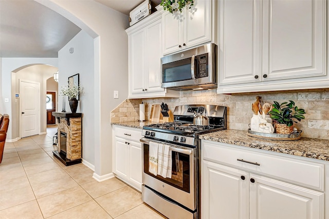 kitchen with light tile patterned flooring, backsplash, appliances with stainless steel finishes, and light stone countertops