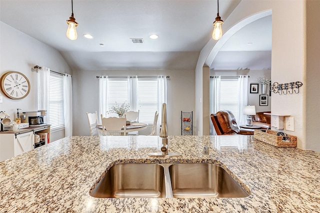 kitchen featuring visible vents, a sink, light stone counters, decorative light fixtures, and arched walkways