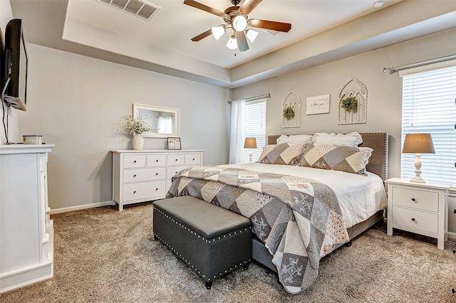 bedroom featuring visible vents, ceiling fan, baseboards, a tray ceiling, and light carpet