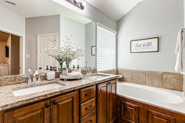 bathroom with a bath, visible vents, double vanity, and a sink