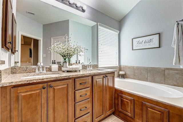 bathroom with double vanity, visible vents, a garden tub, and a sink