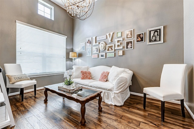 living area featuring baseboards, an inviting chandelier, a towering ceiling, and hardwood / wood-style flooring