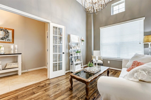 living area with baseboards, a chandelier, french doors, a towering ceiling, and wood finished floors