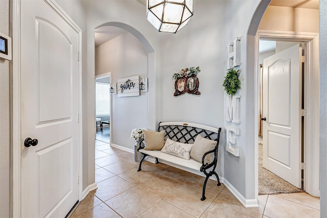 corridor featuring light tile patterned flooring, baseboards, and arched walkways