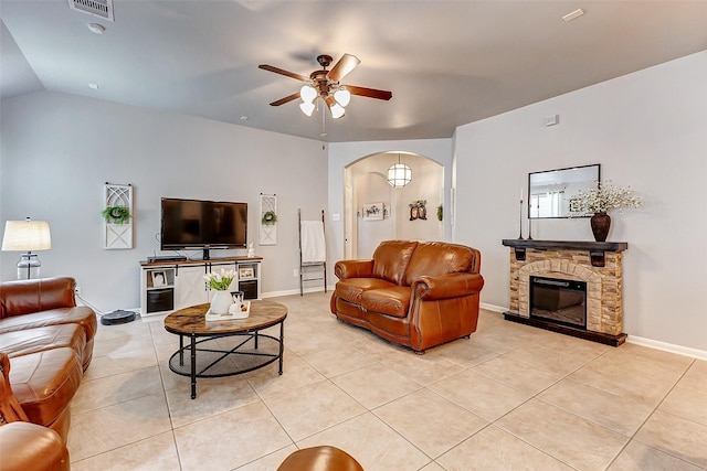 living area featuring a ceiling fan, baseboards, light tile patterned flooring, arched walkways, and a stone fireplace