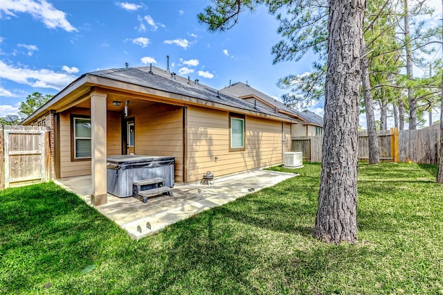 back of house with a fenced backyard, a lawn, a hot tub, and a patio