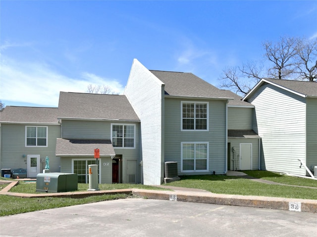 view of front facade featuring central AC unit, roof with shingles, and a front lawn