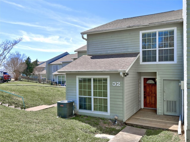 exterior space with central AC unit, roof with shingles, and a lawn