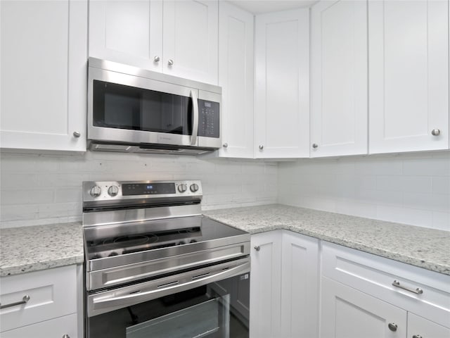 kitchen with stainless steel appliances, white cabinetry, decorative backsplash, and light stone counters