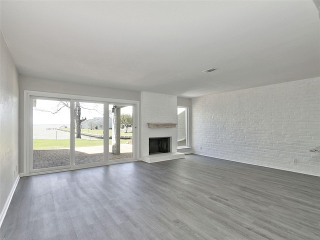 unfurnished living room with baseboards, visible vents, a large fireplace, and wood finished floors