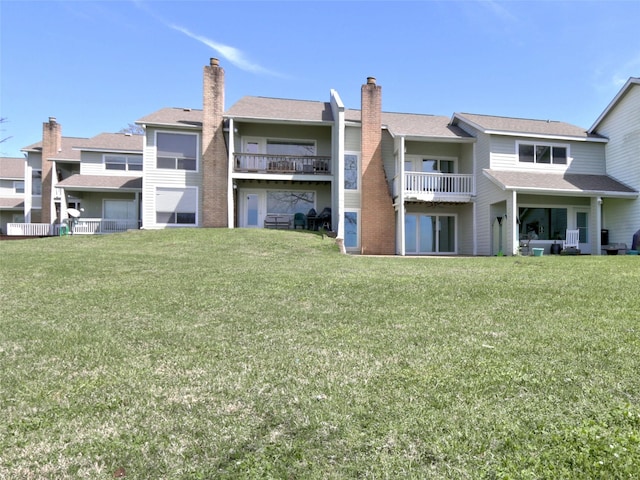 back of property featuring a balcony, a chimney, and a lawn
