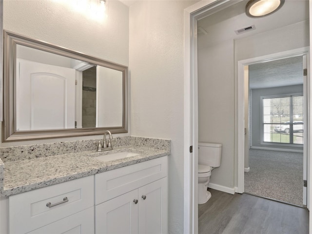 bathroom featuring toilet, baseboards, visible vents, vanity, and wood finished floors