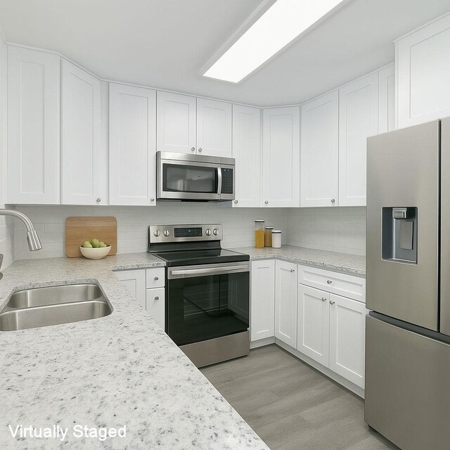 kitchen with light wood-style flooring, a sink, white cabinetry, tasteful backsplash, and appliances with stainless steel finishes