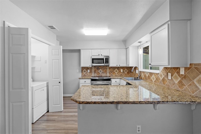 kitchen with a sink, light stone counters, washer / clothes dryer, appliances with stainless steel finishes, and a peninsula