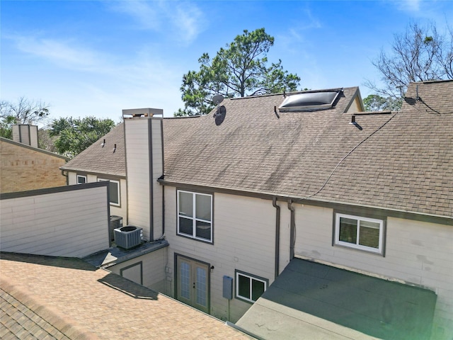 rear view of property with a shingled roof, central air condition unit, french doors, a chimney, and a patio