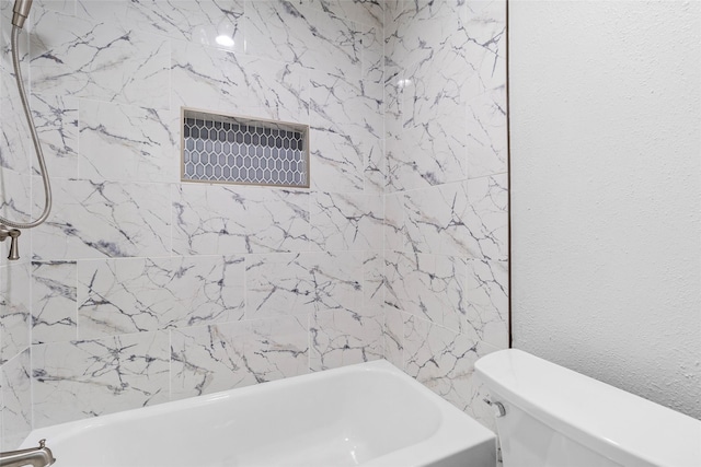 bathroom featuring toilet, shower / bath combination, and a textured wall