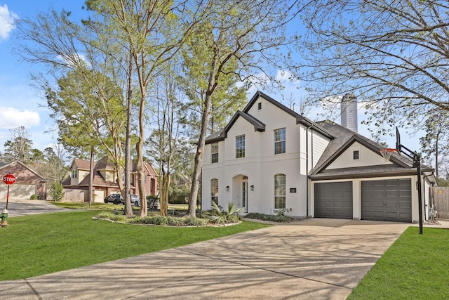 view of front facade with concrete driveway, a front yard, stucco siding, a chimney, and a garage