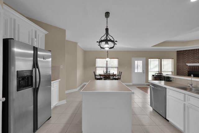 kitchen with light tile patterned floors, a kitchen island, a sink, stainless steel appliances, and white cabinets