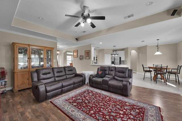 living area with a tray ceiling, wood finished floors, arched walkways, and baseboards