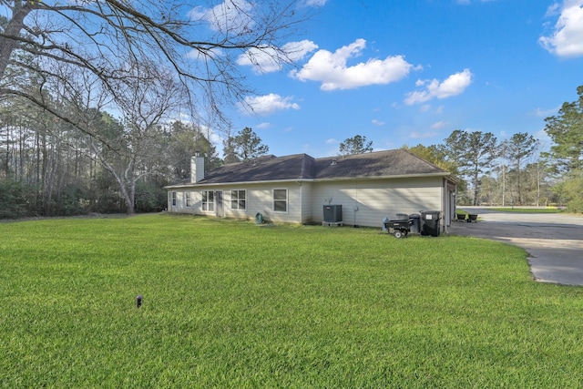 back of property with central AC unit, driveway, a chimney, and a yard