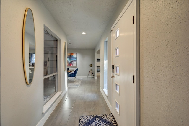 corridor with recessed lighting, baseboards, a textured ceiling, and wood finished floors