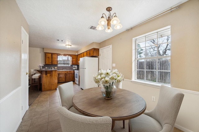 dining area featuring light tile patterned floors, visible vents, a textured ceiling, and a notable chandelier