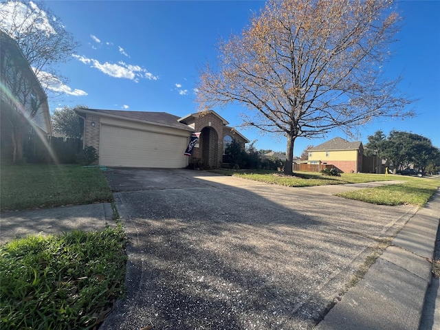 single story home with a front lawn, driveway, fence, an attached garage, and brick siding