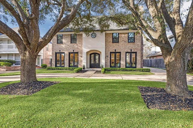 view of front of house with brick siding, french doors, a front yard, and fence