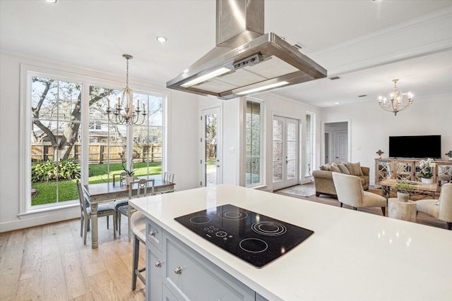 kitchen with a notable chandelier, light wood-style flooring, island range hood, light countertops, and black electric stovetop