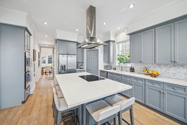 kitchen featuring a breakfast bar area, island exhaust hood, a sink, appliances with stainless steel finishes, and crown molding