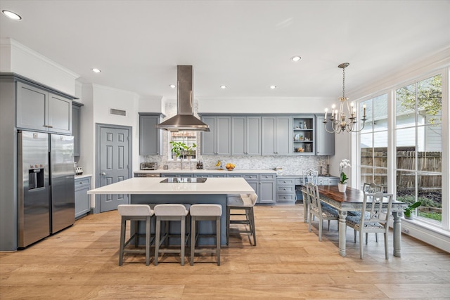 kitchen featuring decorative backsplash, gray cabinets, stainless steel refrigerator with ice dispenser, and island range hood