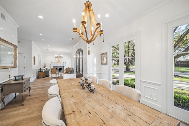 dining space featuring a fireplace, recessed lighting, ornamental molding, light wood-style floors, and a chandelier