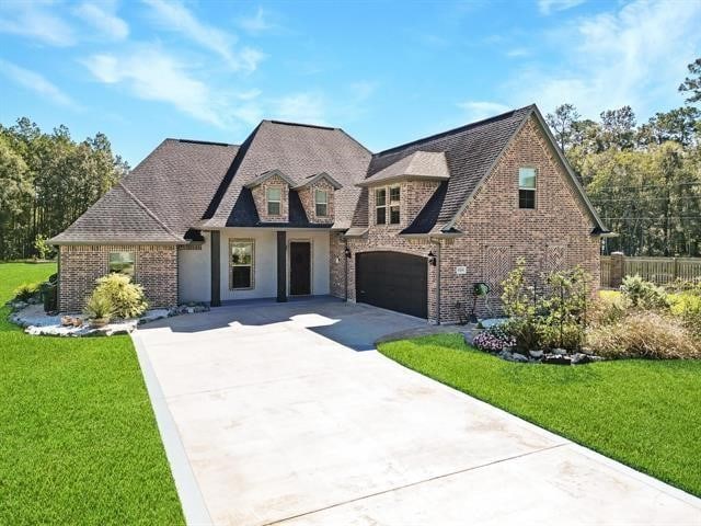 french country inspired facade featuring brick siding, driveway, and a front lawn