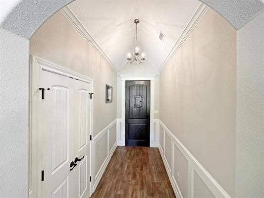 doorway to outside with dark wood-style floors, crown molding, a decorative wall, a chandelier, and vaulted ceiling