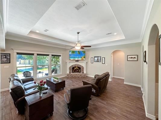 living area featuring a tray ceiling, wood finished floors, and arched walkways