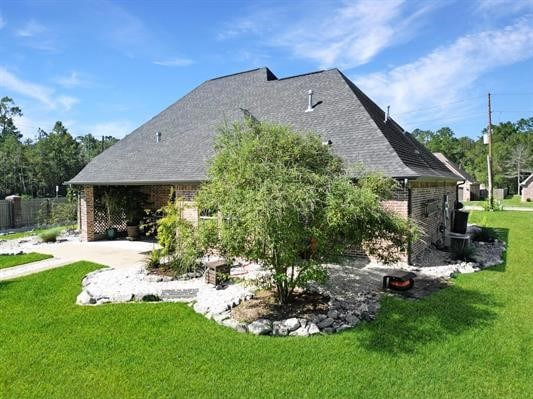 rear view of property featuring a lawn, roof with shingles, and brick siding