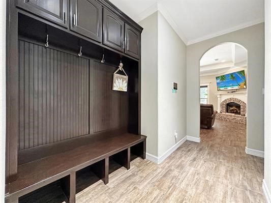 mudroom featuring arched walkways, light wood-style floors, a fireplace, crown molding, and baseboards