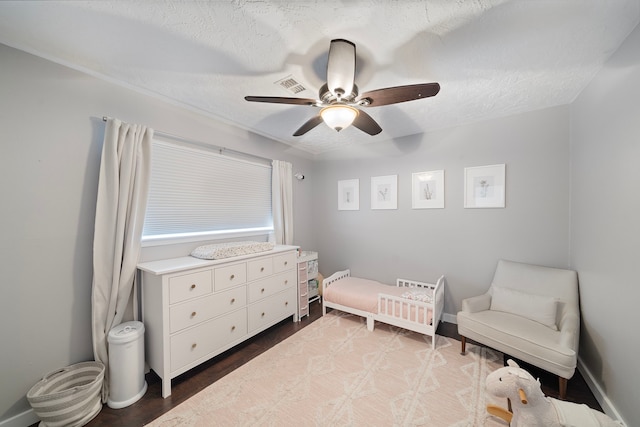 bedroom with wood finished floors, a ceiling fan, visible vents, a nursery area, and a textured ceiling