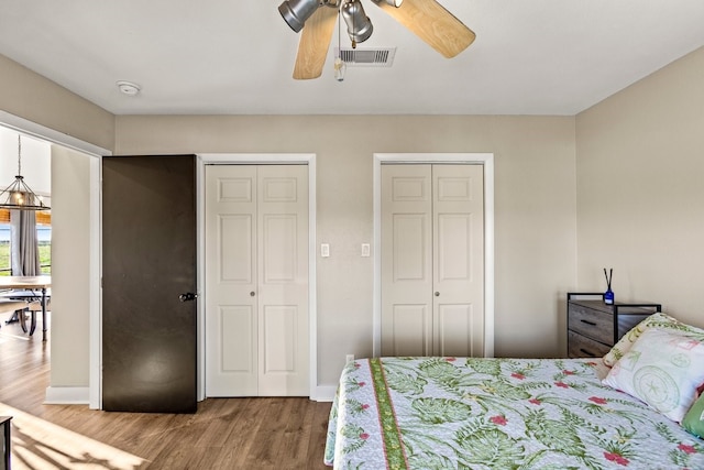 bedroom featuring a ceiling fan, baseboards, wood finished floors, visible vents, and multiple closets