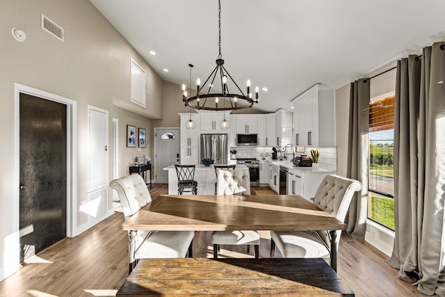 dining space with light wood finished floors, visible vents, recessed lighting, a high ceiling, and an inviting chandelier