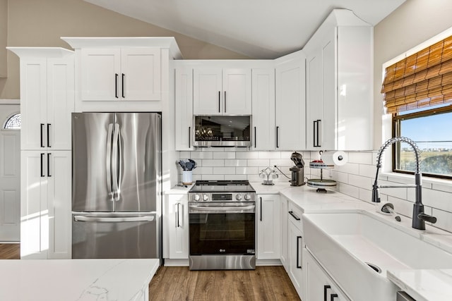 kitchen featuring a sink, tasteful backsplash, wood finished floors, stainless steel appliances, and vaulted ceiling