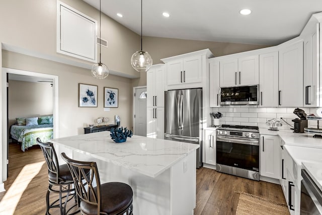 kitchen with a kitchen island, stainless steel appliances, vaulted ceiling, dark wood-type flooring, and tasteful backsplash