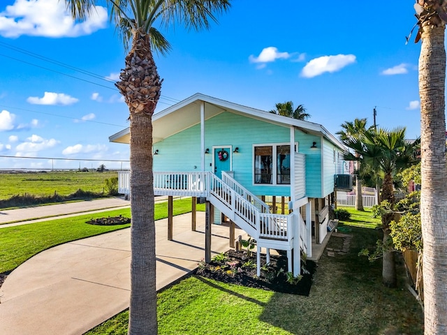 coastal inspired home with stairway, central AC unit, a porch, and a front lawn